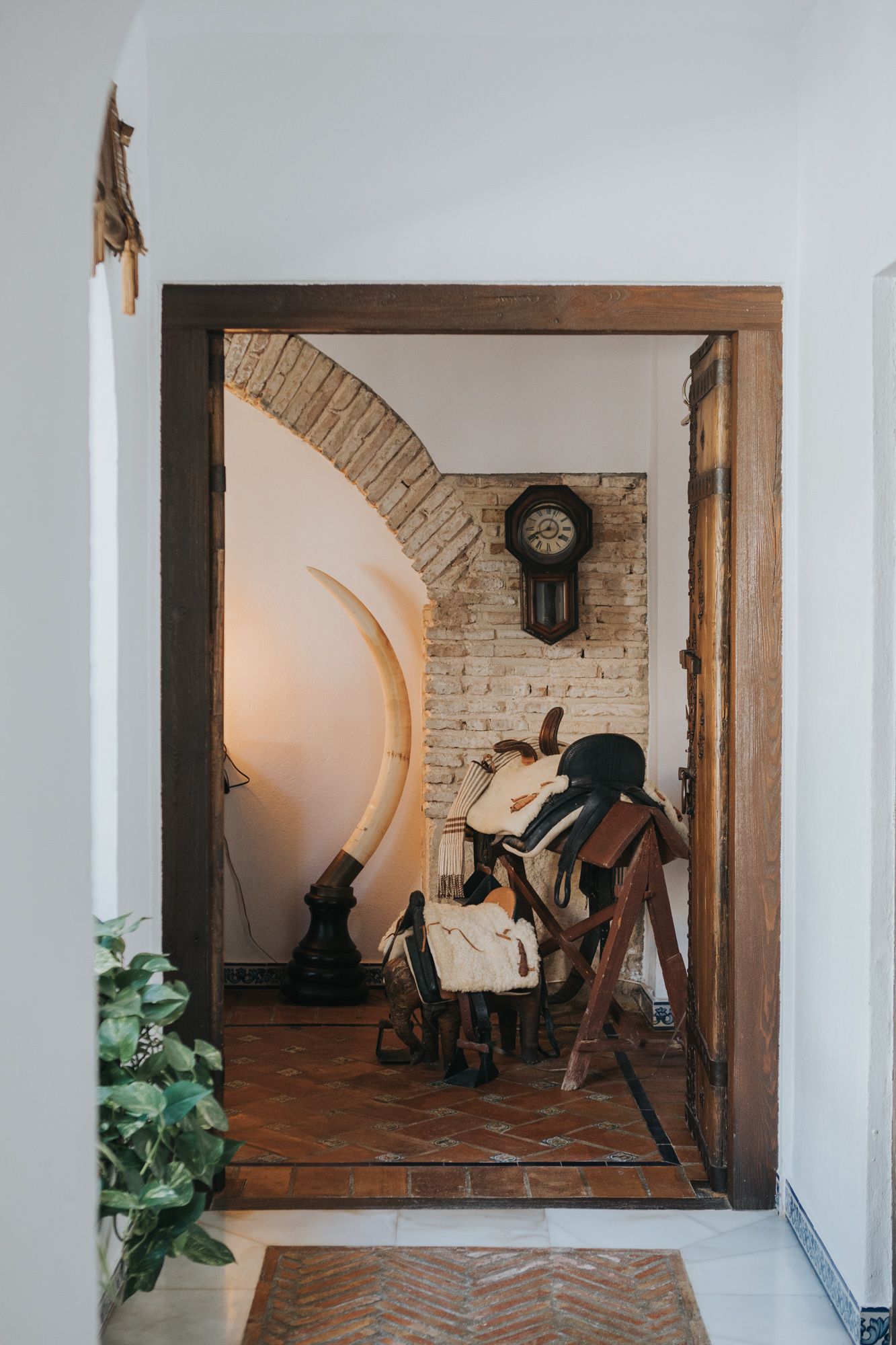 Rustic interior doorway with saddle display, brick arch, and vintage pendulum clock.