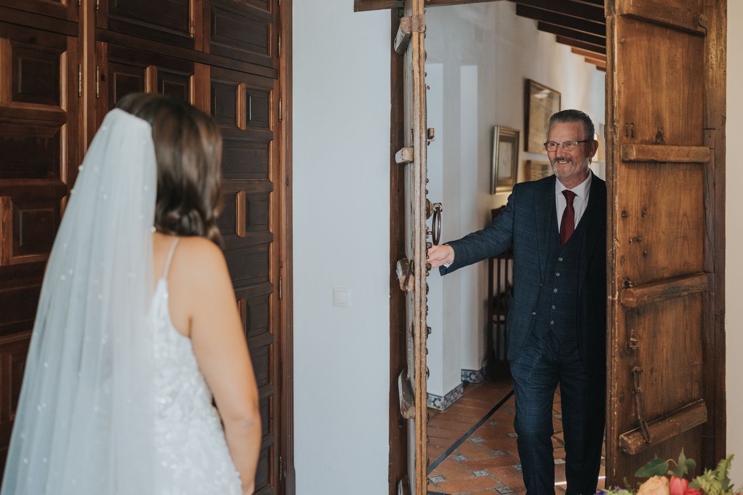 A candid first look moment between a bride and groom through a wooden doorway.