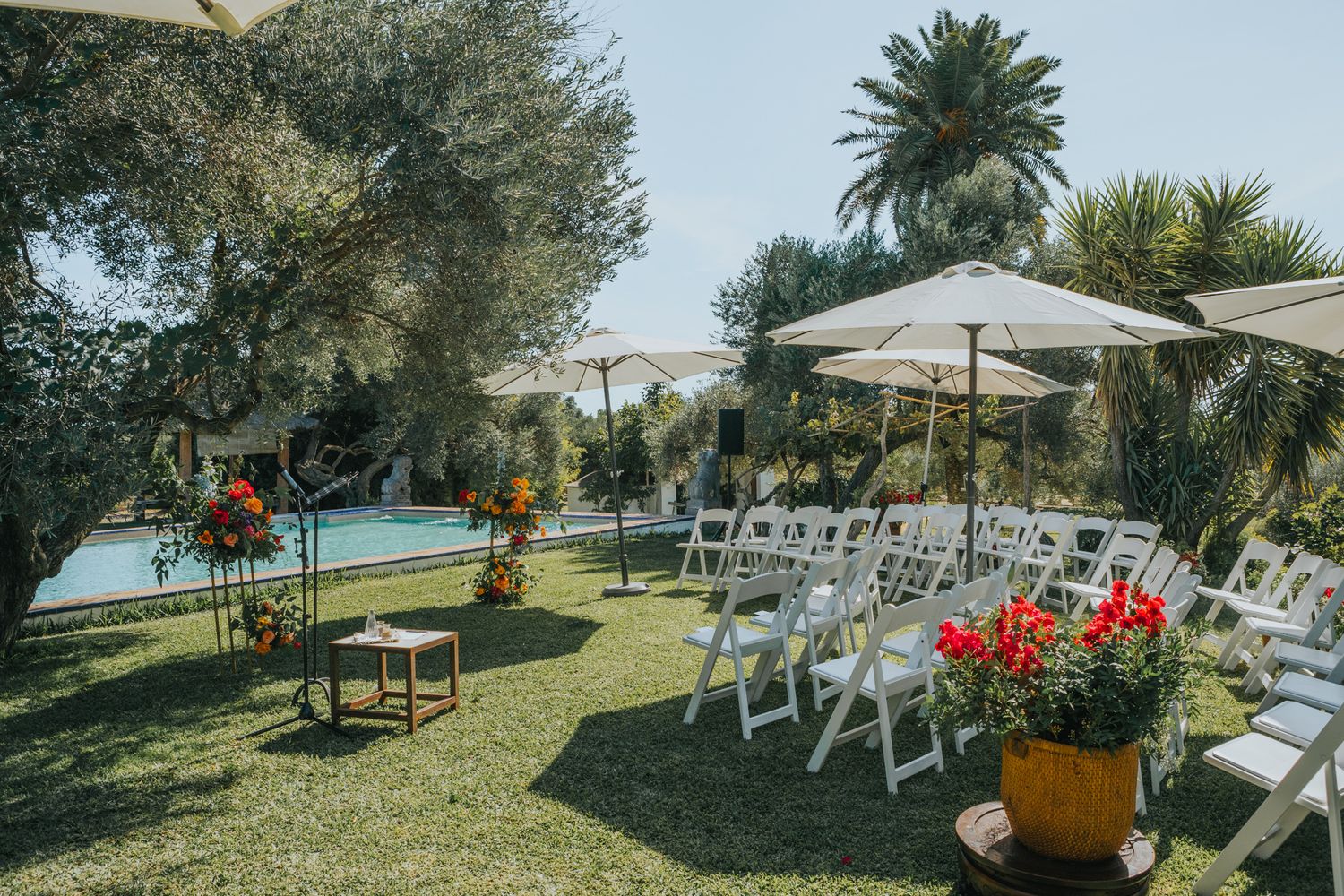 Outdoor wedding ceremony setup with white chairs and floral decorations next to a swimming pool.