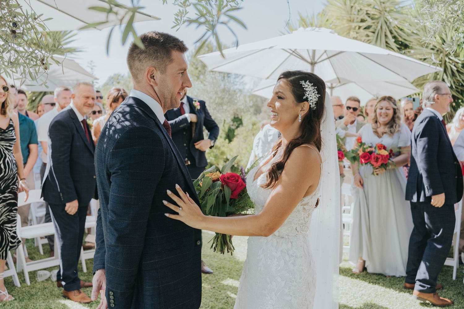 An outdoor wedding ceremony under white umbrellas with vibrant floral bouquets.