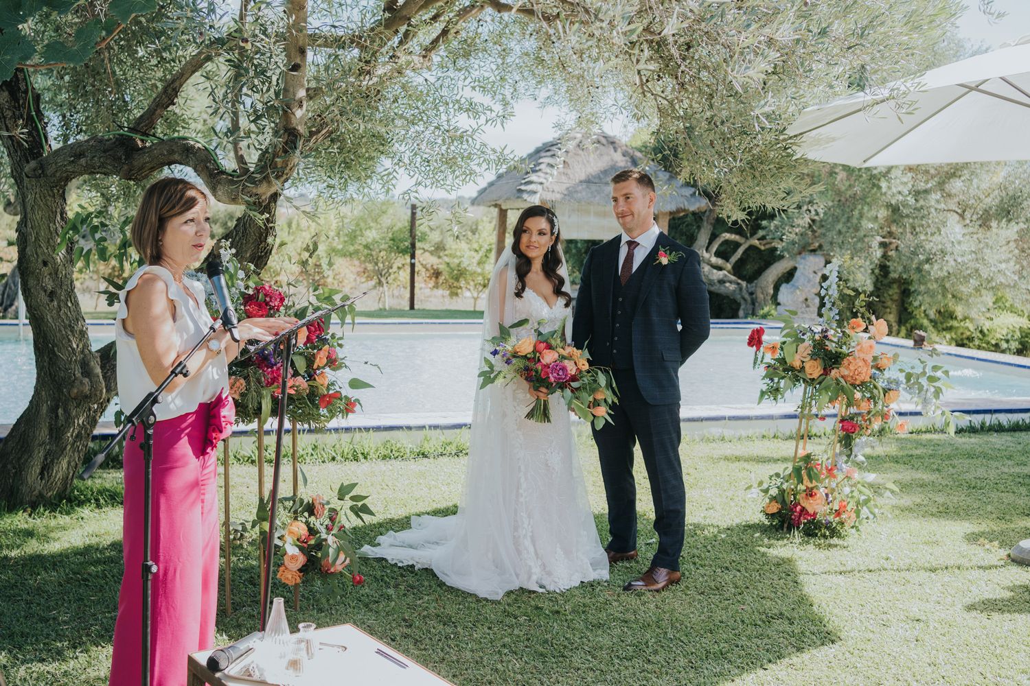 Outdoor wedding ceremony setup with floral arrangements and white umbrellas under trees.