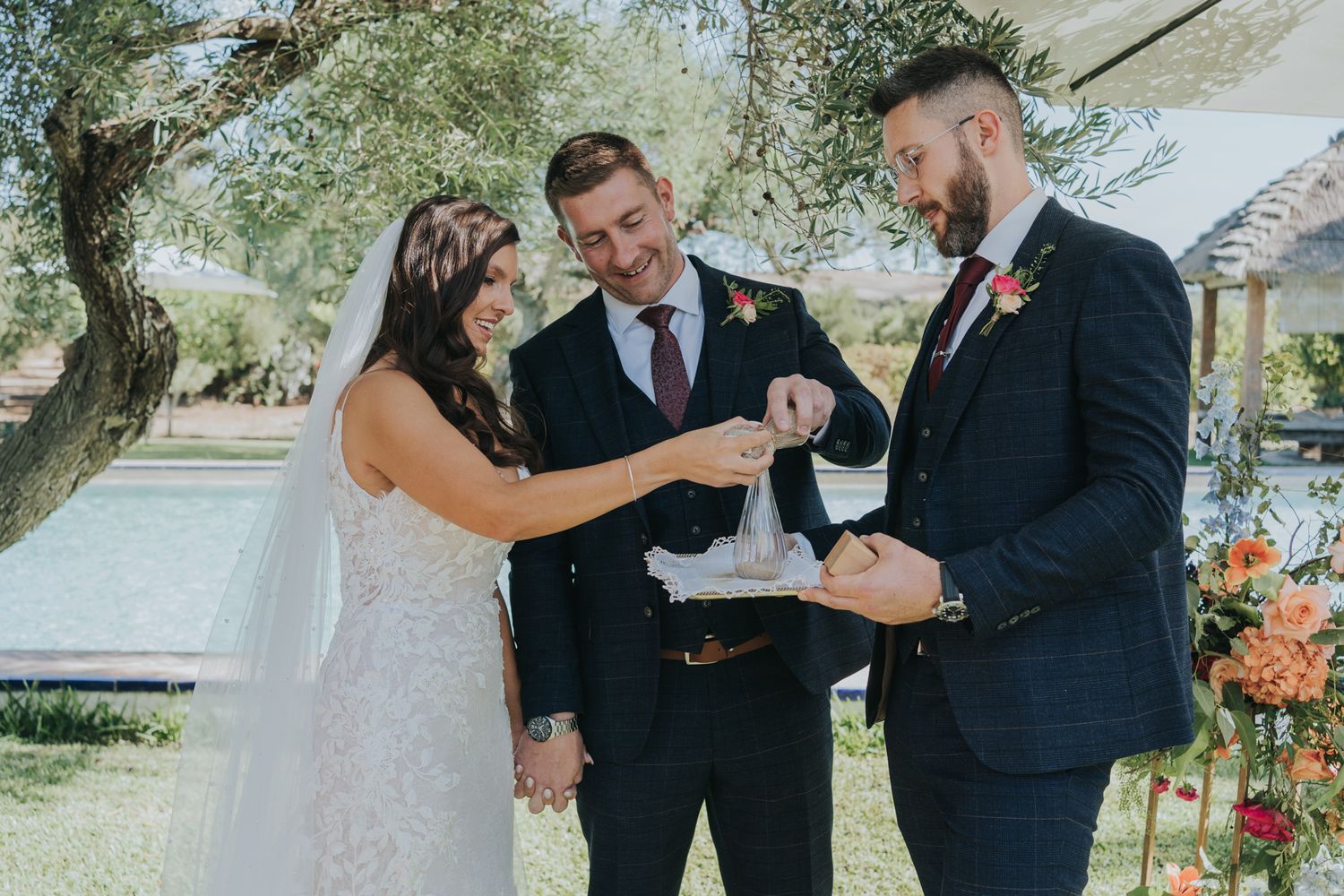 A joyful outdoor wedding ceremony with exchange of rings under trees and floral decorations.