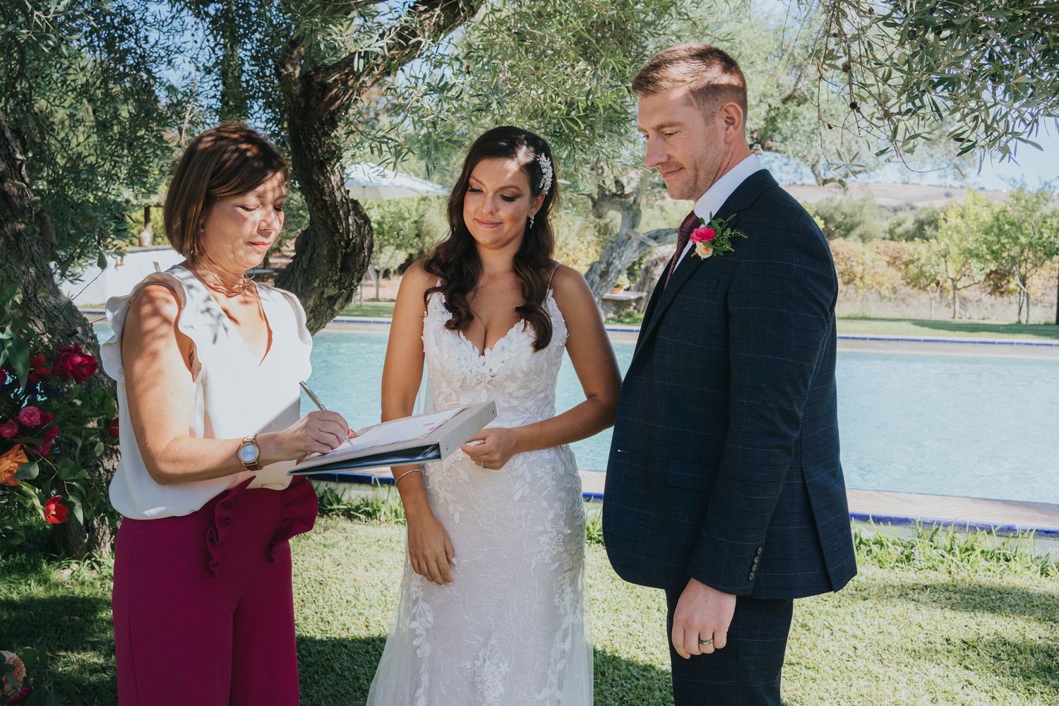 An outdoor wedding ceremony taking place under trees with an officiant leading the service.