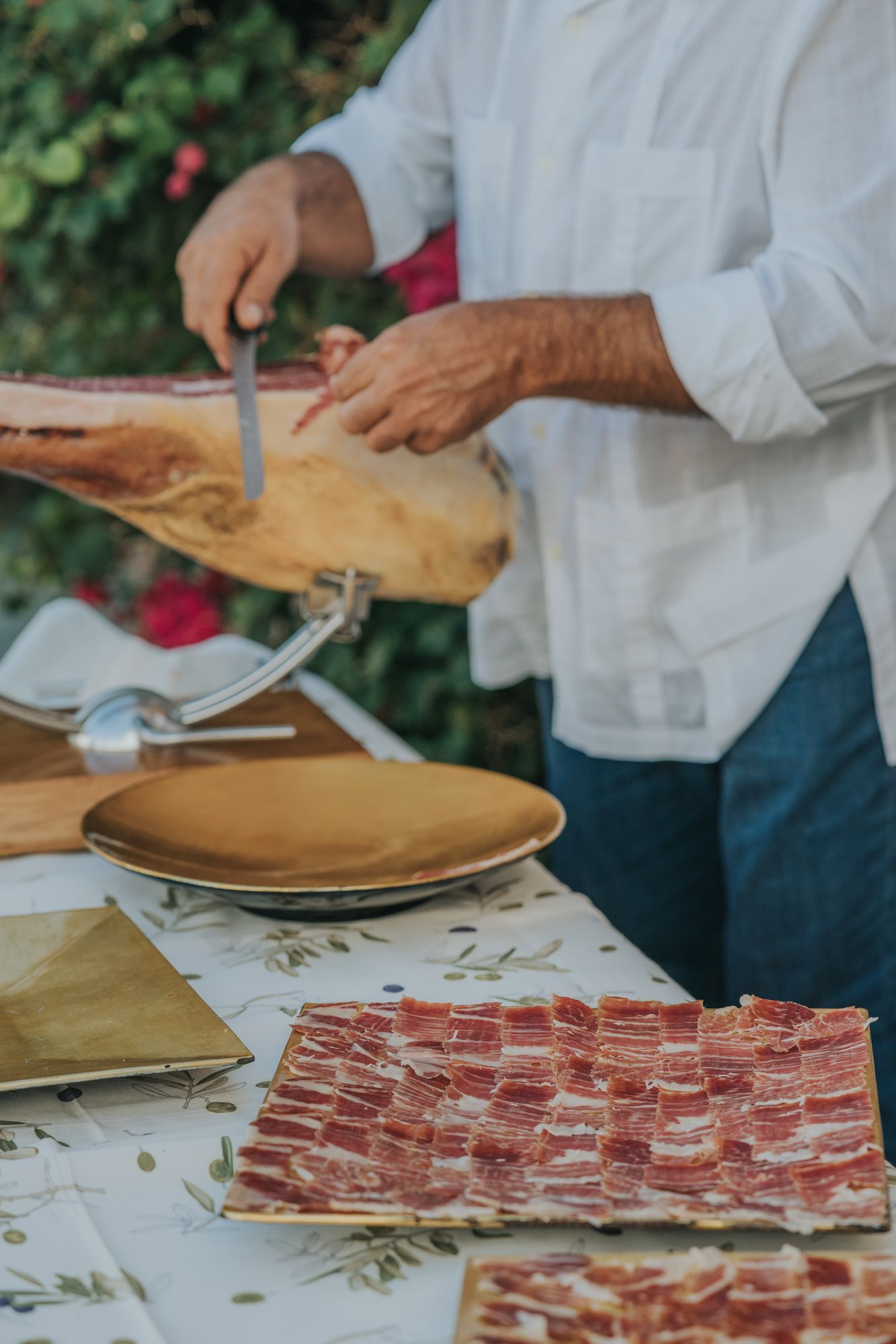 Fresh plates of thinly sliced cured ham being prepared on a decorated table with white linens.