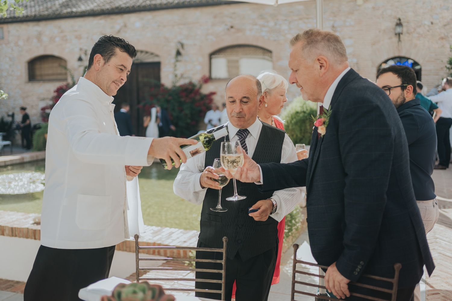 Wedding guests toasting with champagne glasses at an elegant venue with stone architecture.