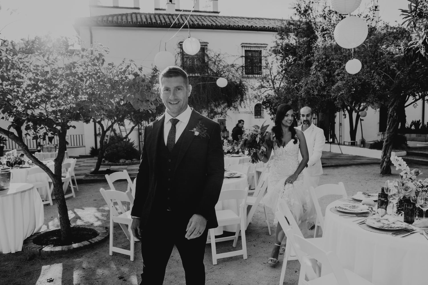 A black and white photo of a wedding reception setup with outdoor tables and string lights.