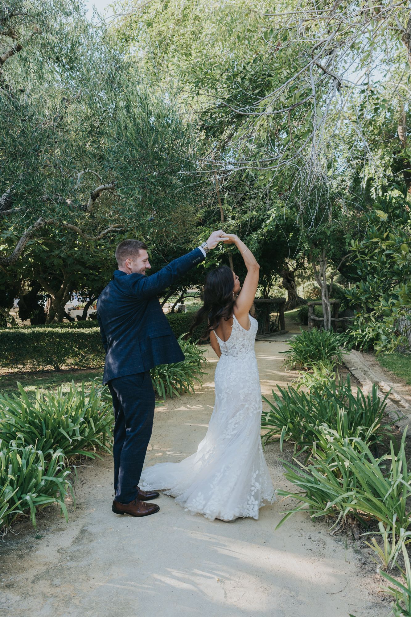 Wedding couple dancing together on a garden path surrounded by trees and iris plants.