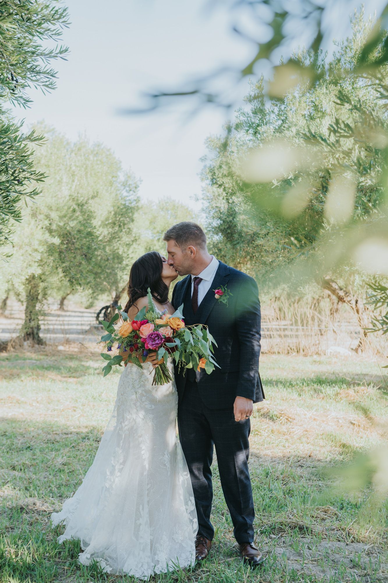 Romantic wedding moment in an olive grove with vibrant floral bouquet.