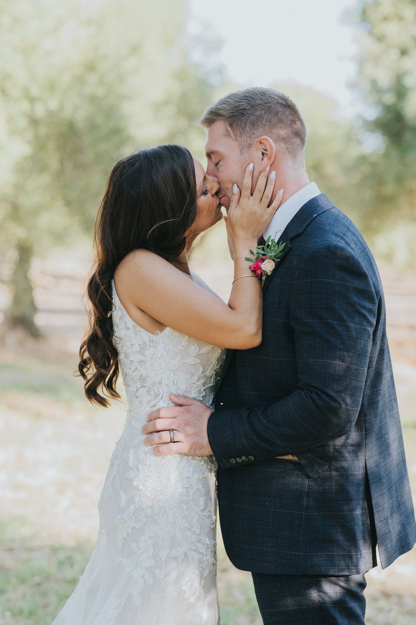 Wedding couple sharing an intimate romantic kiss outdoors with soft natural lighting and greenery in background.
