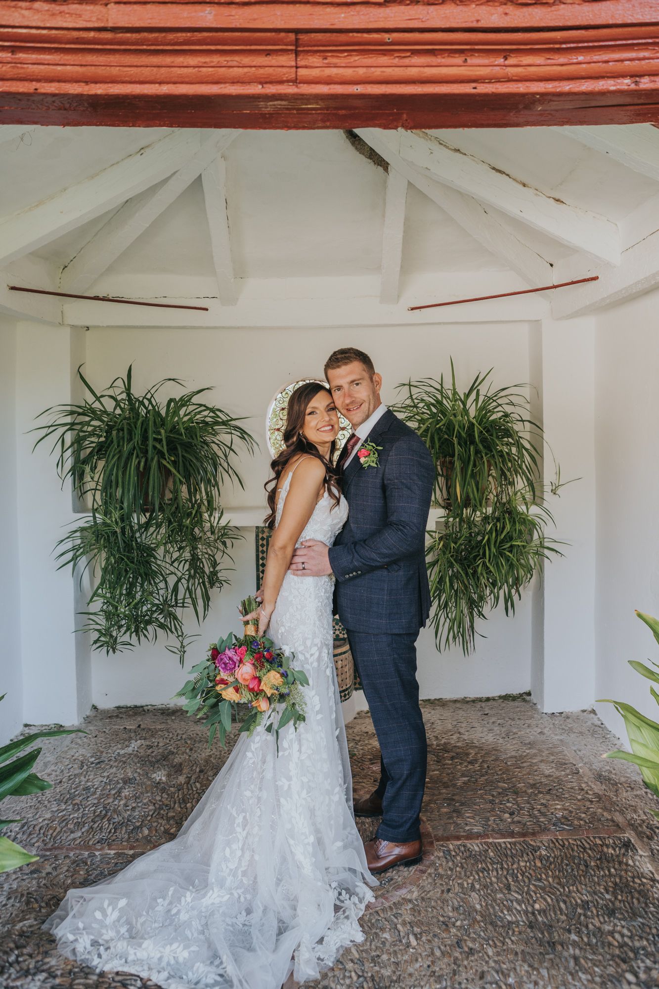 A romantic wedding portrait in a white gazebo with tropical plants and a trailing lace gown.