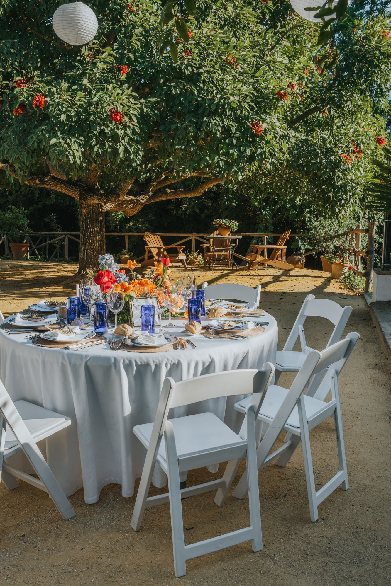 Elegant outdoor wedding reception table setting with white linens, blue accents and paper lantern decorations.