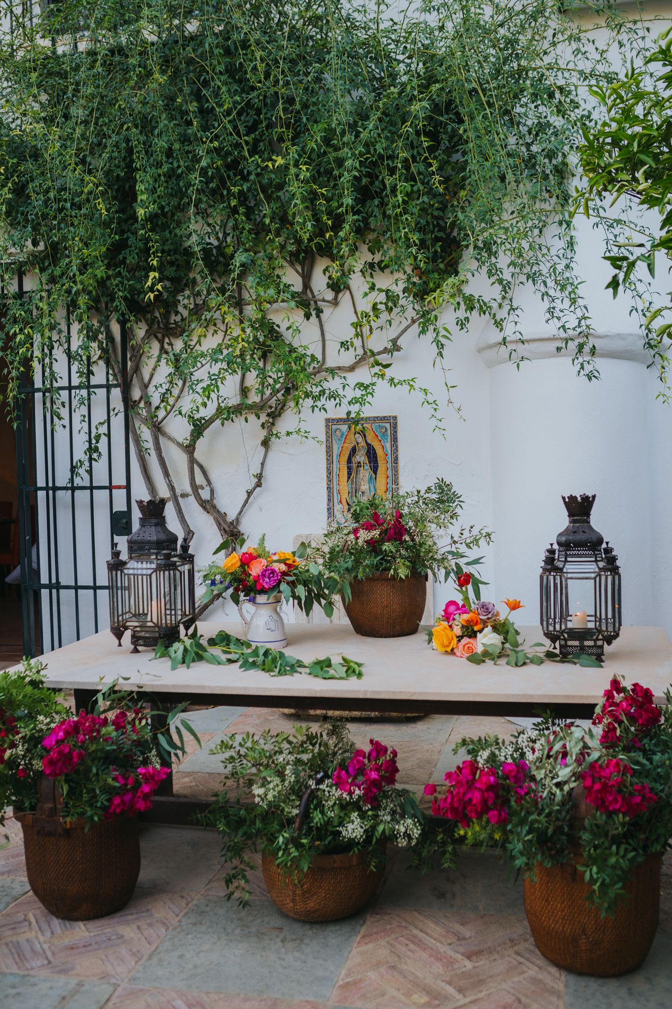 Beautiful courtyard garden setup with lanterns, potted flowers and a rustic table decorated with vibrant floral arrangements.