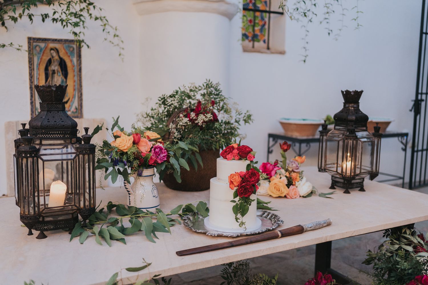 Romantic wedding decor display with vintage lanterns, fresh flowers and greenery arranged on white table.