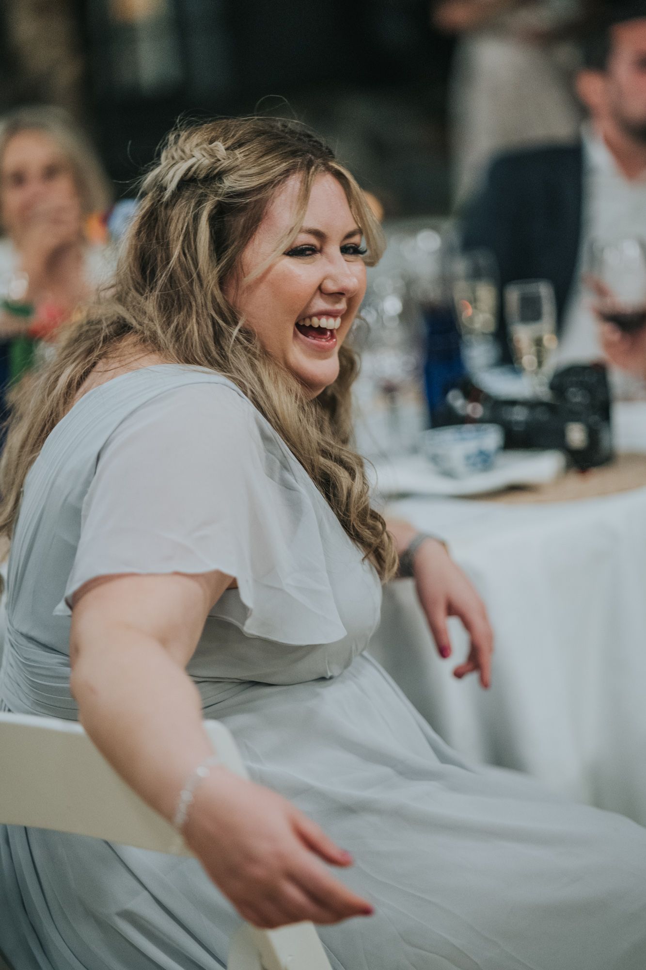 Guest at a wedding reception wearing a light gray dress appears to be enjoying a candid moment at the dinner table.