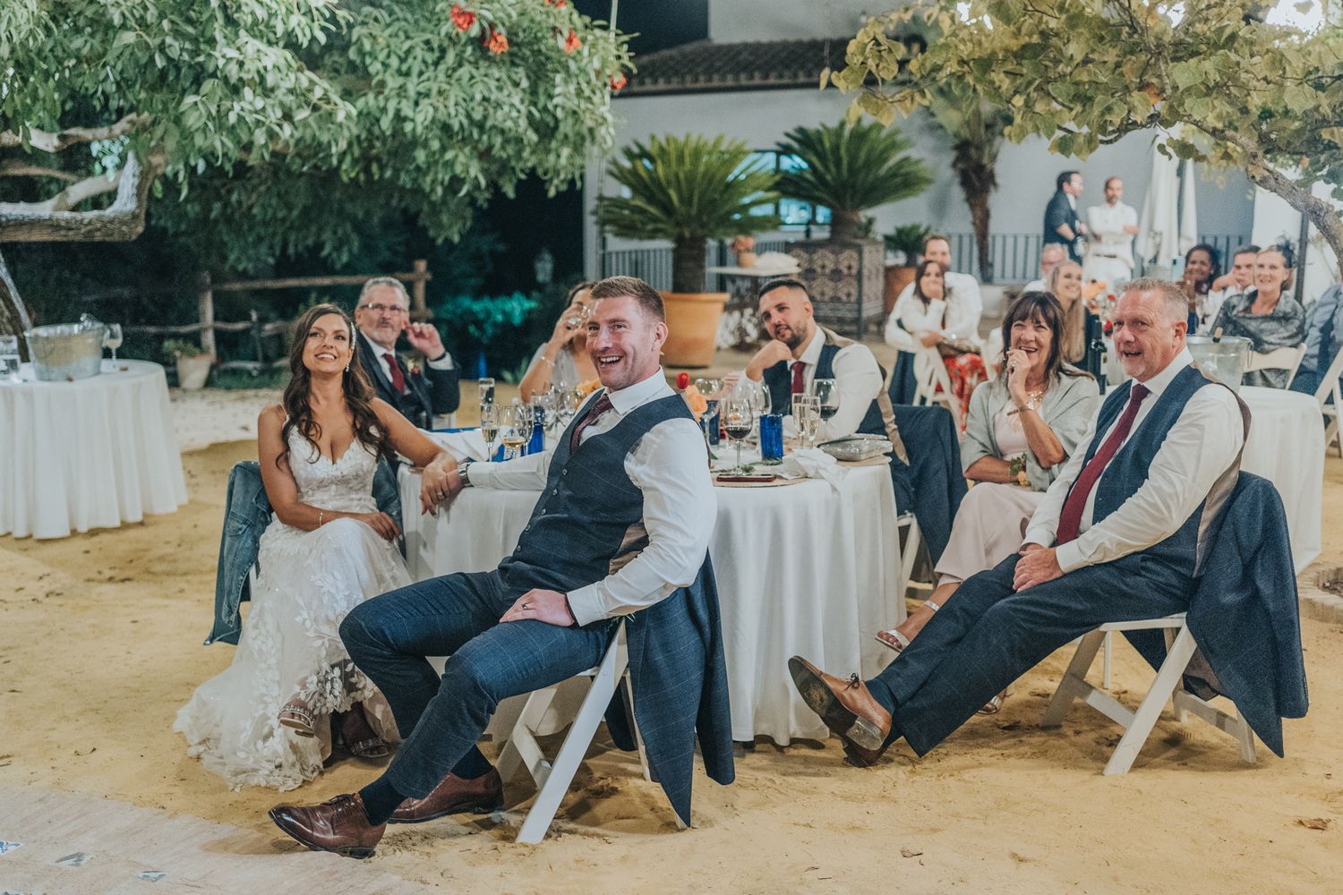 Wedding guests enjoying an outdoor reception with table seating at a rustic venue.