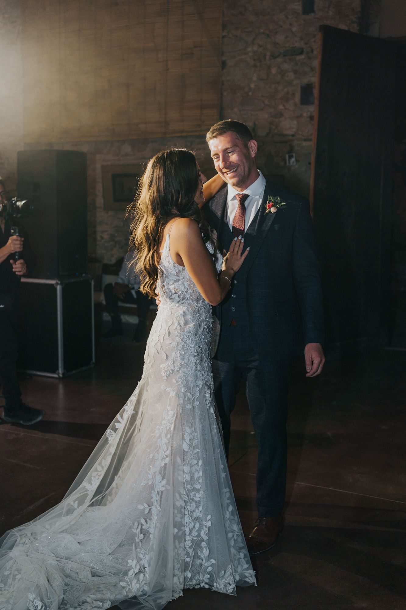 Romantic first dance moment between newlyweds in an elegant rustic venue with brick walls.