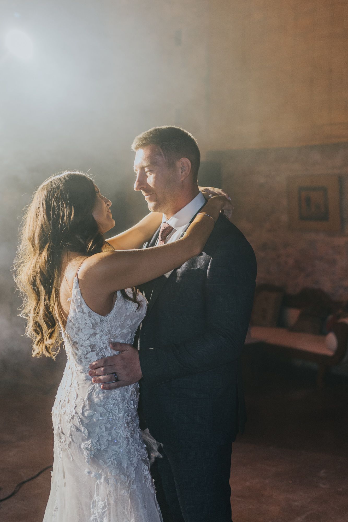 A romantic first dance moment between newlyweds as dramatic light streams through the hazy room.