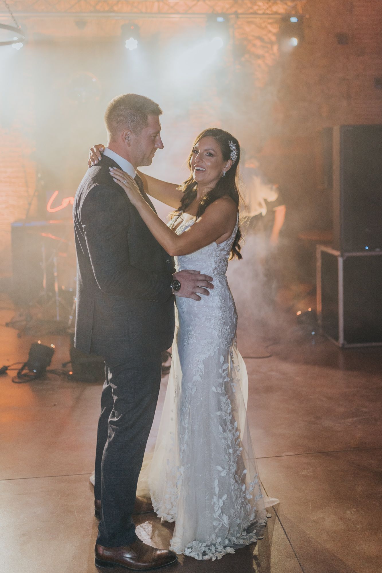 A couple shares their first dance at their wedding reception surrounded by atmospheric fog and lighting.
