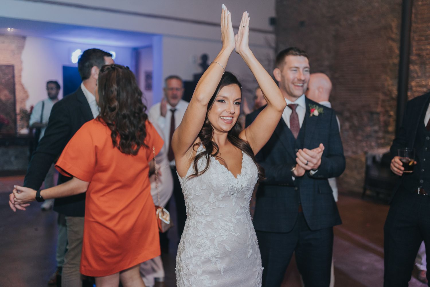 Wedding celebration on the dance floor with guests dancing and celebrating in a brick-walled venue.