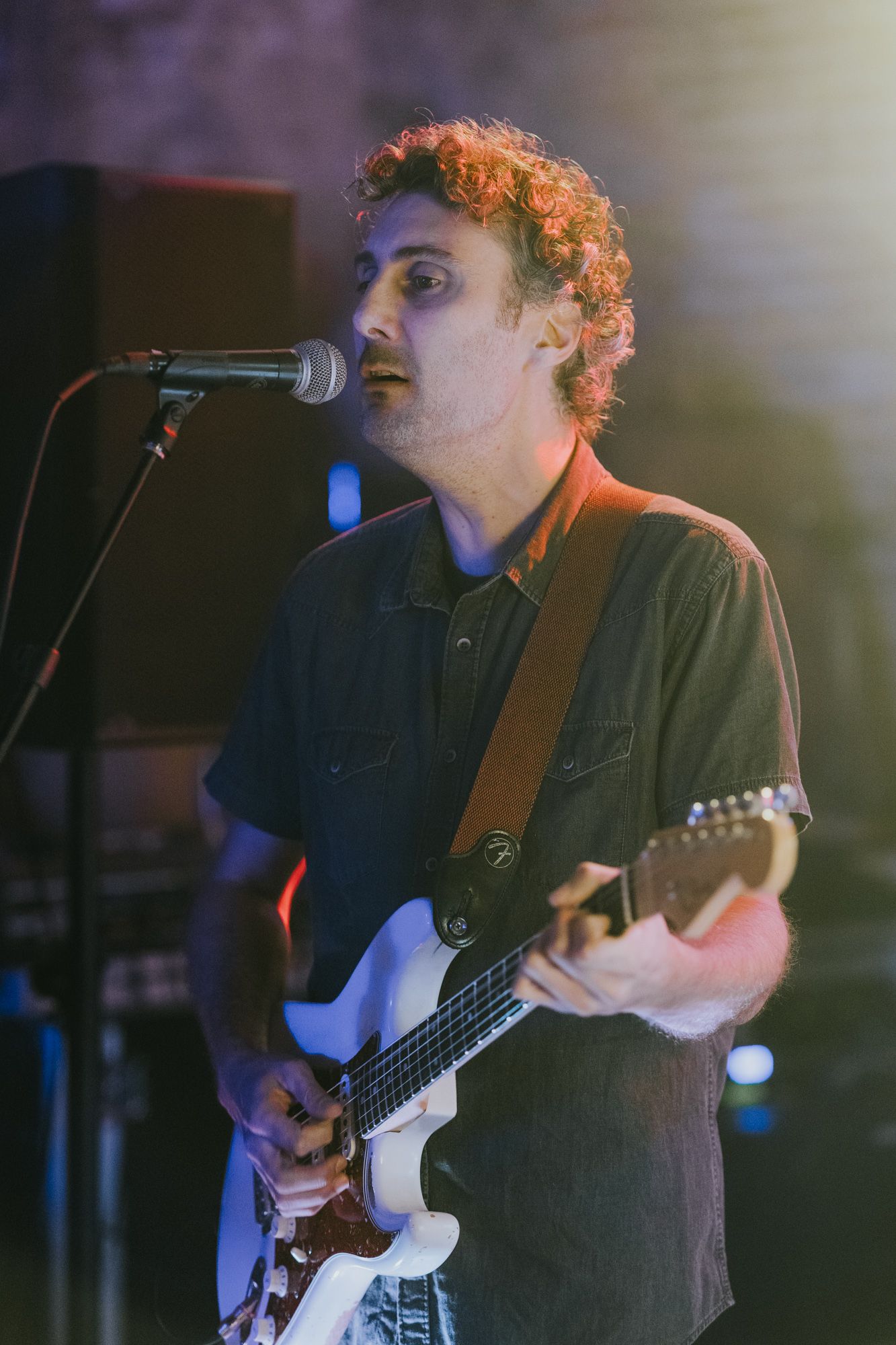 Musician plays electric guitar and sings into microphone during live performance.