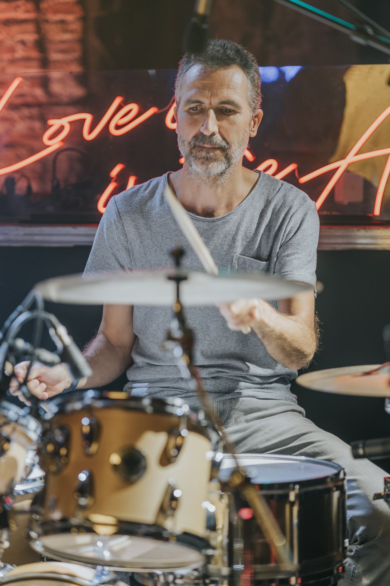 Drummer performs on stage with neon lighting and signage in background.