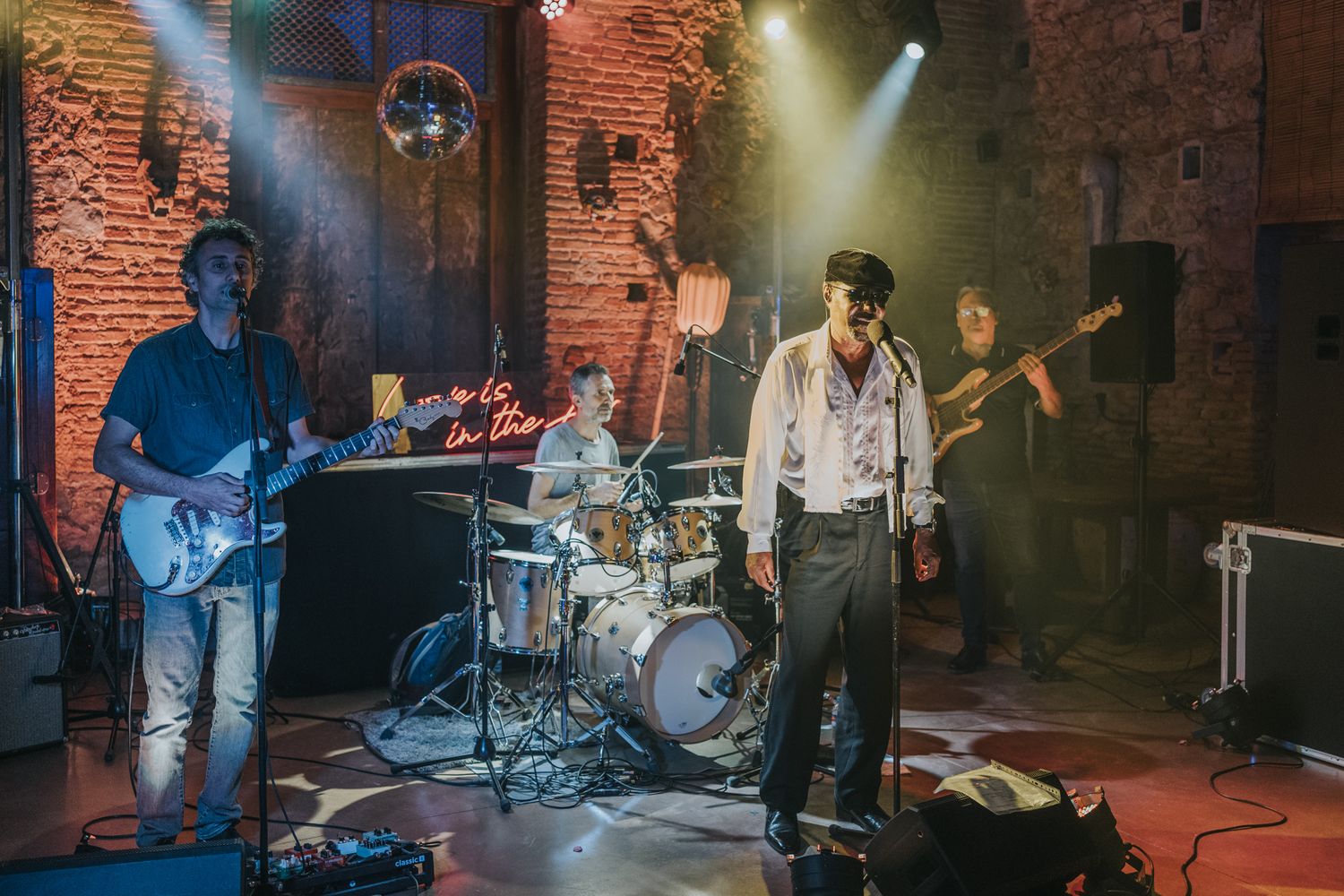 A band performs on stage in a rustic brick venue with dramatic lighting and a disco ball overhead.