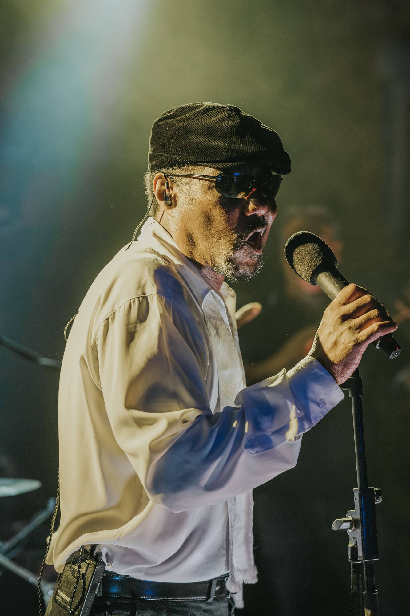 A performer in a cap and white shirt sings passionately into a microphone on stage.