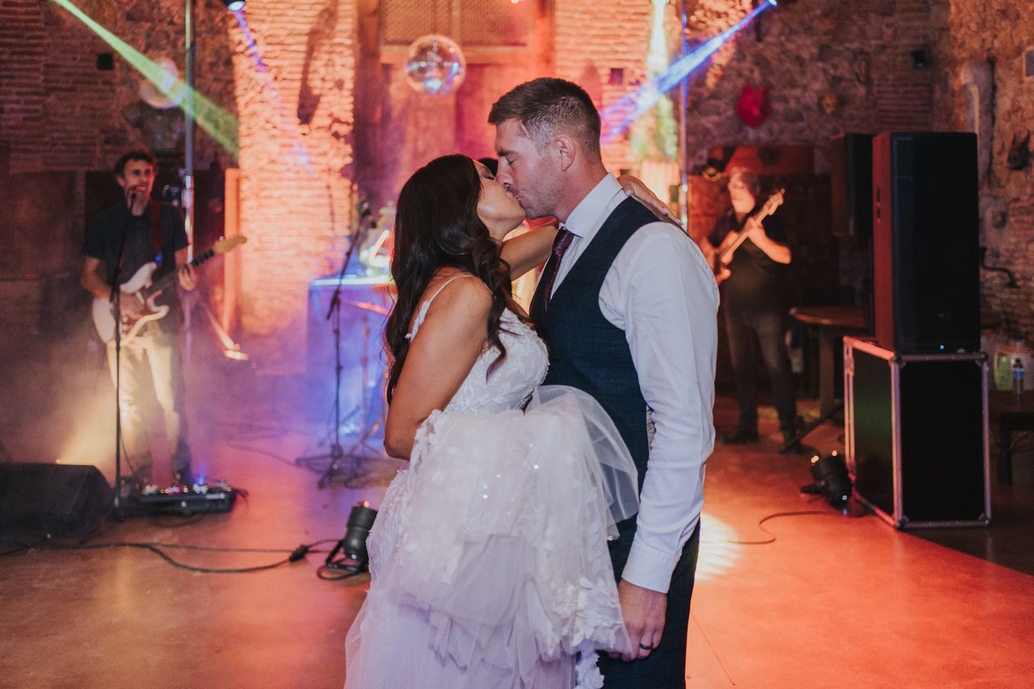 A couple shares their first dance at a wedding reception in a brick-walled venue with dramatic orange lighting.