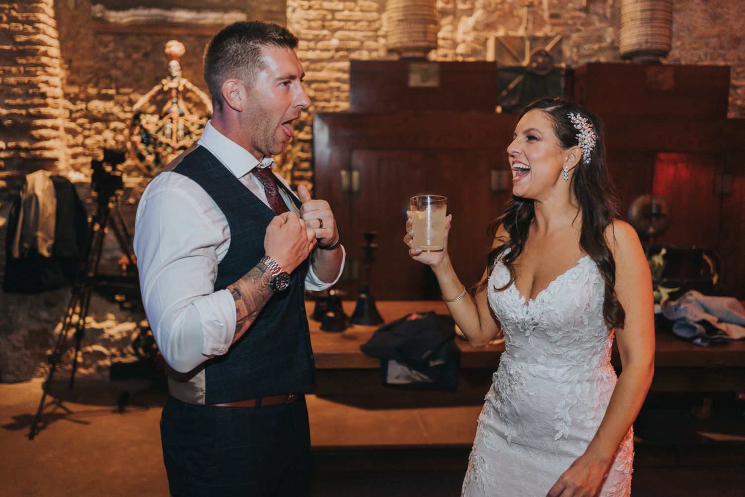 Couple in wedding attire dance and laugh together at their reception in a rustic brick venue.