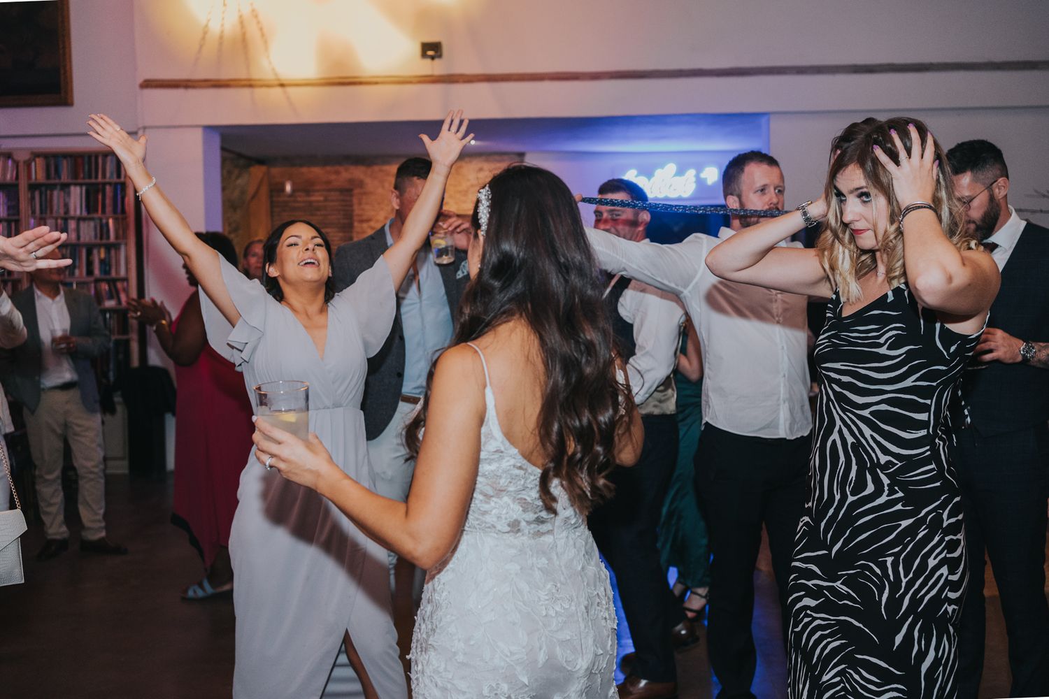 Wedding reception guests dancing and celebrating on a dimly lit dance floor.