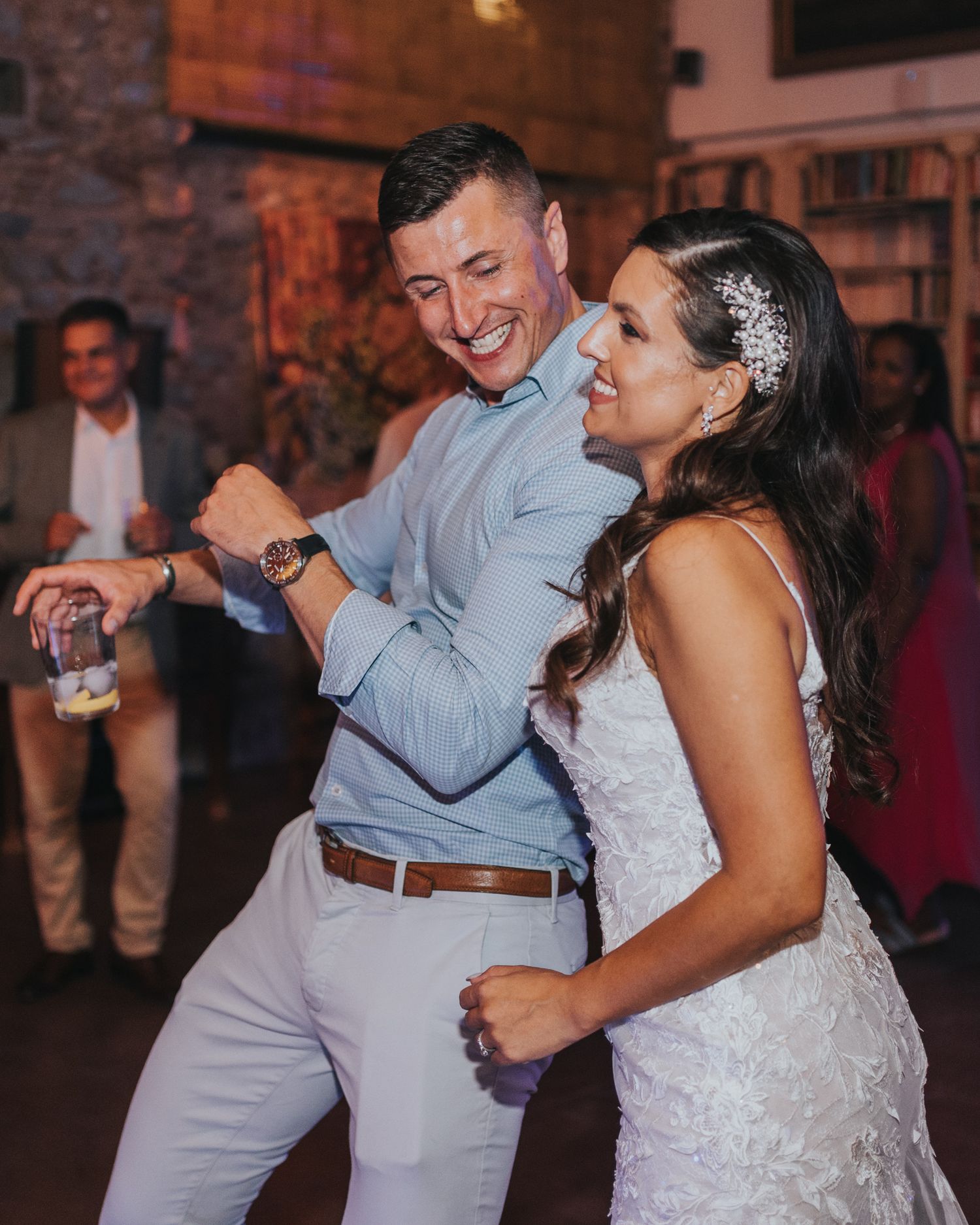A couple dances joyfully at a wedding reception, with the bride wearing a white lace dress and sparkly hair accessory.