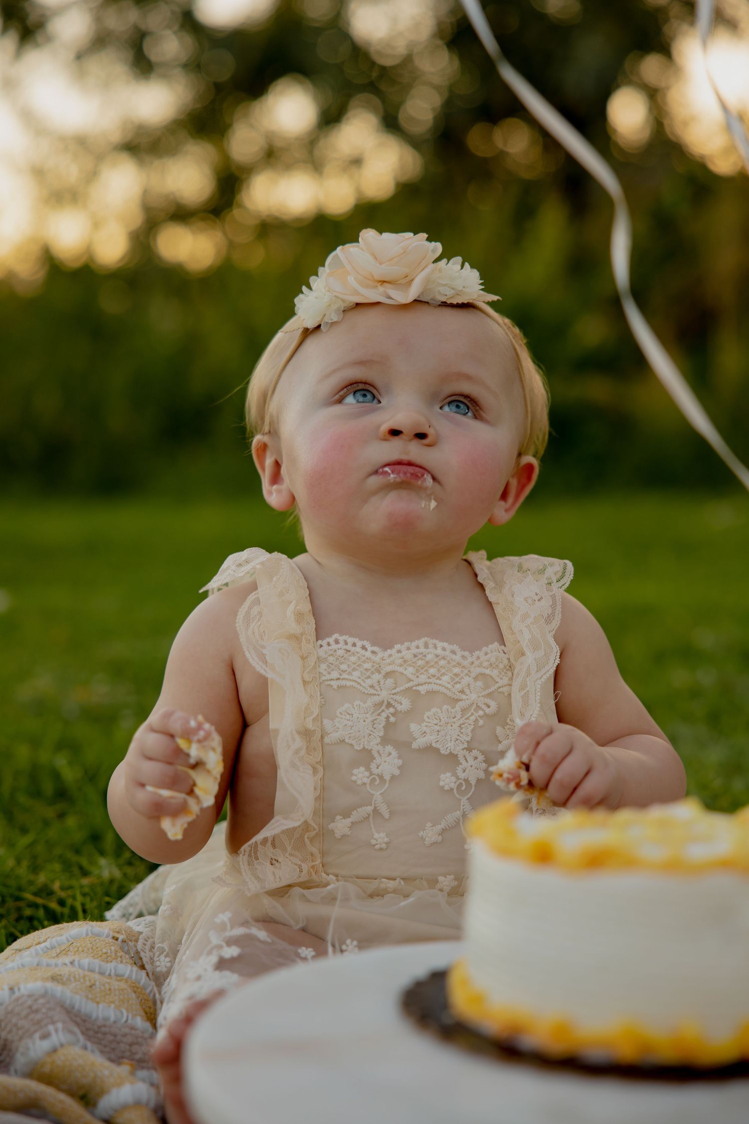 A charming cake smash photo session with delicate lace outfit and yellow cake outdoors.