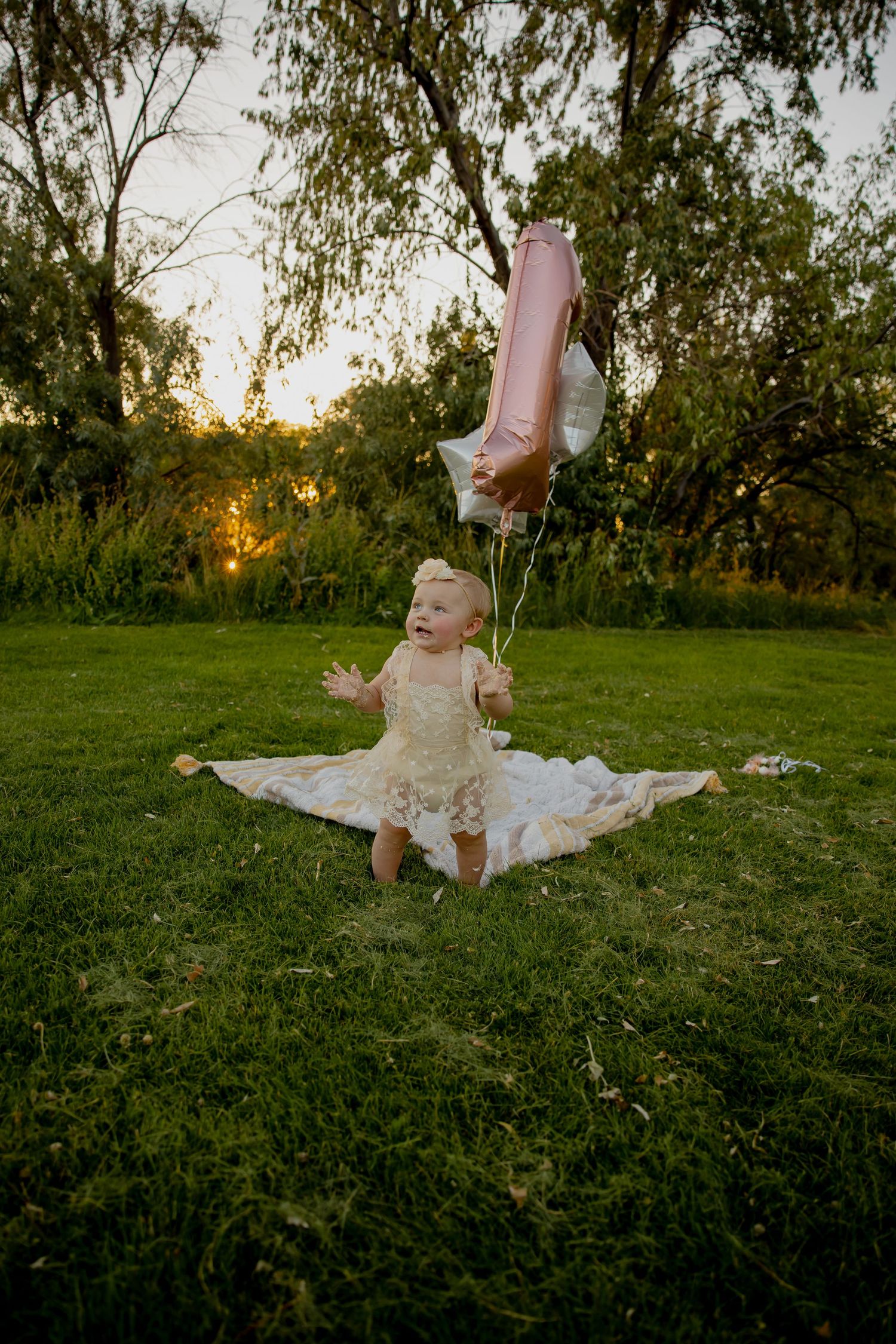 Garden party setup with pink balloons and white decorations on a blanket at sunset.