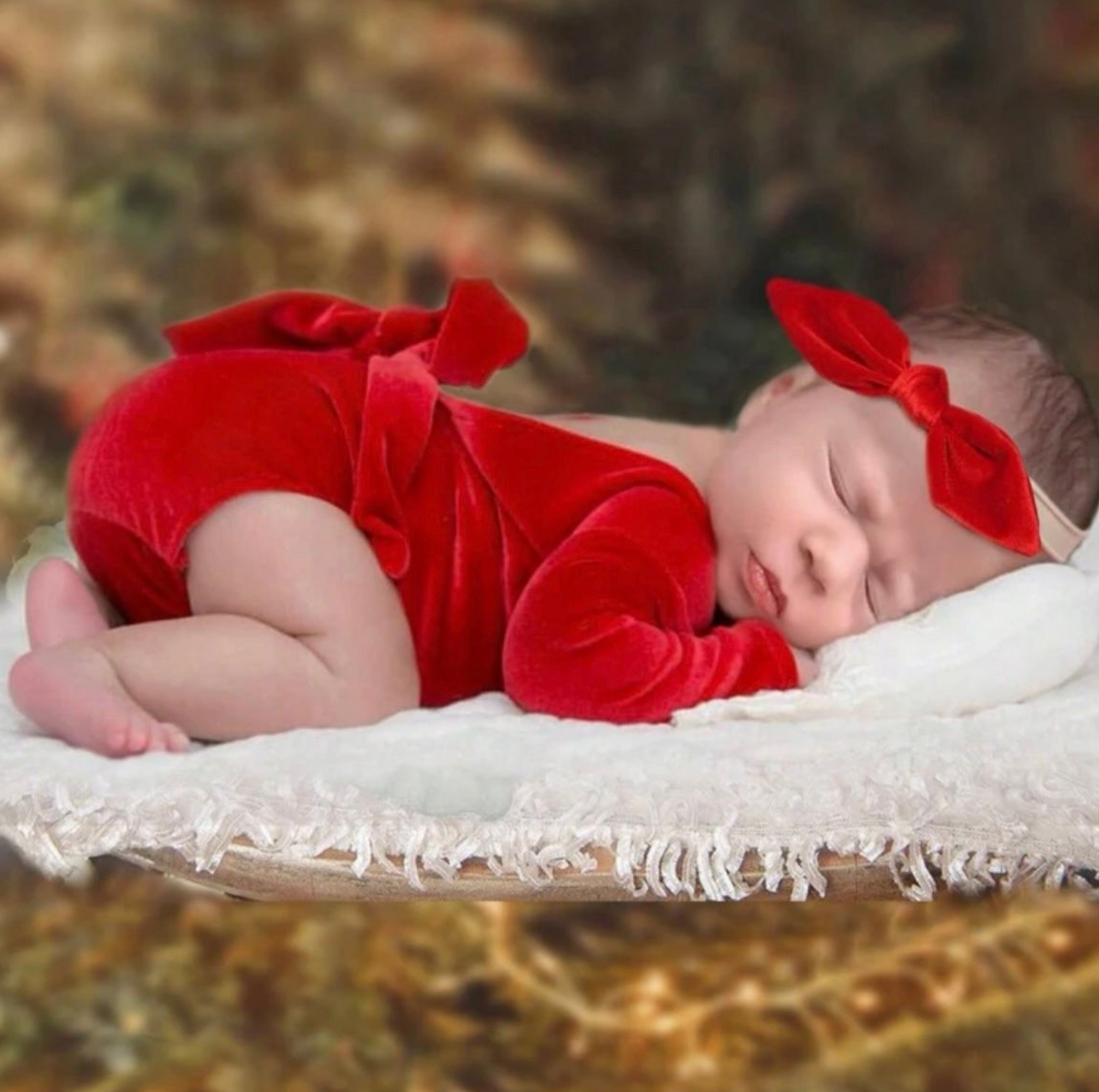 Baby in red dress sleeping peacefully on white textured blanket.