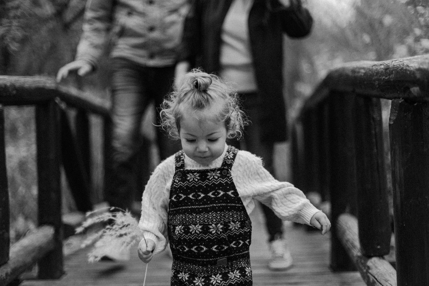 18 months old girl walking though a bridge in front of her parents at the park, in Toronto