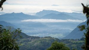 Rolling hills and mountain peaks visible through scattered clouds in daytime landscape.