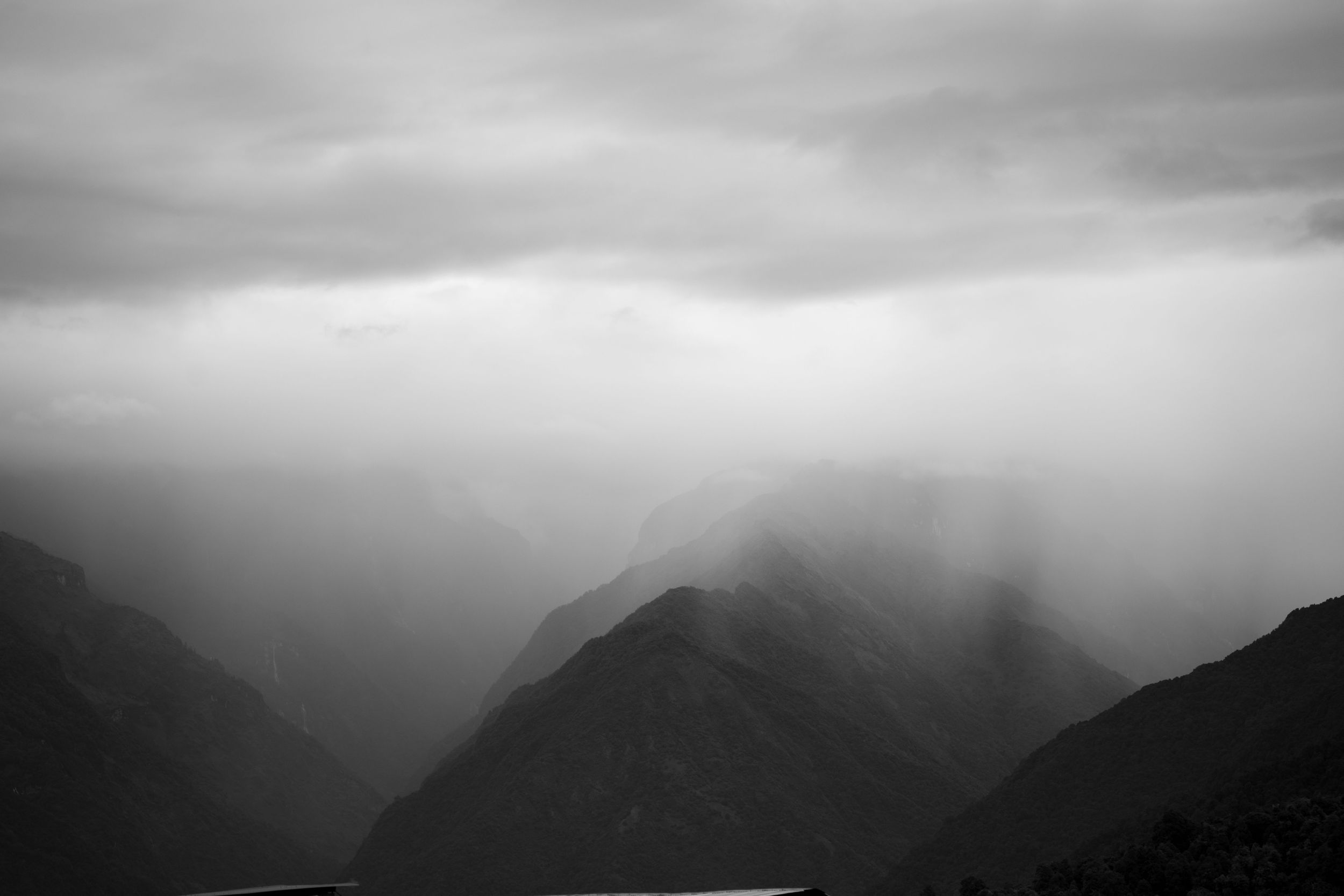 Moody black and white mountain landscape with fog rolling through valleys.