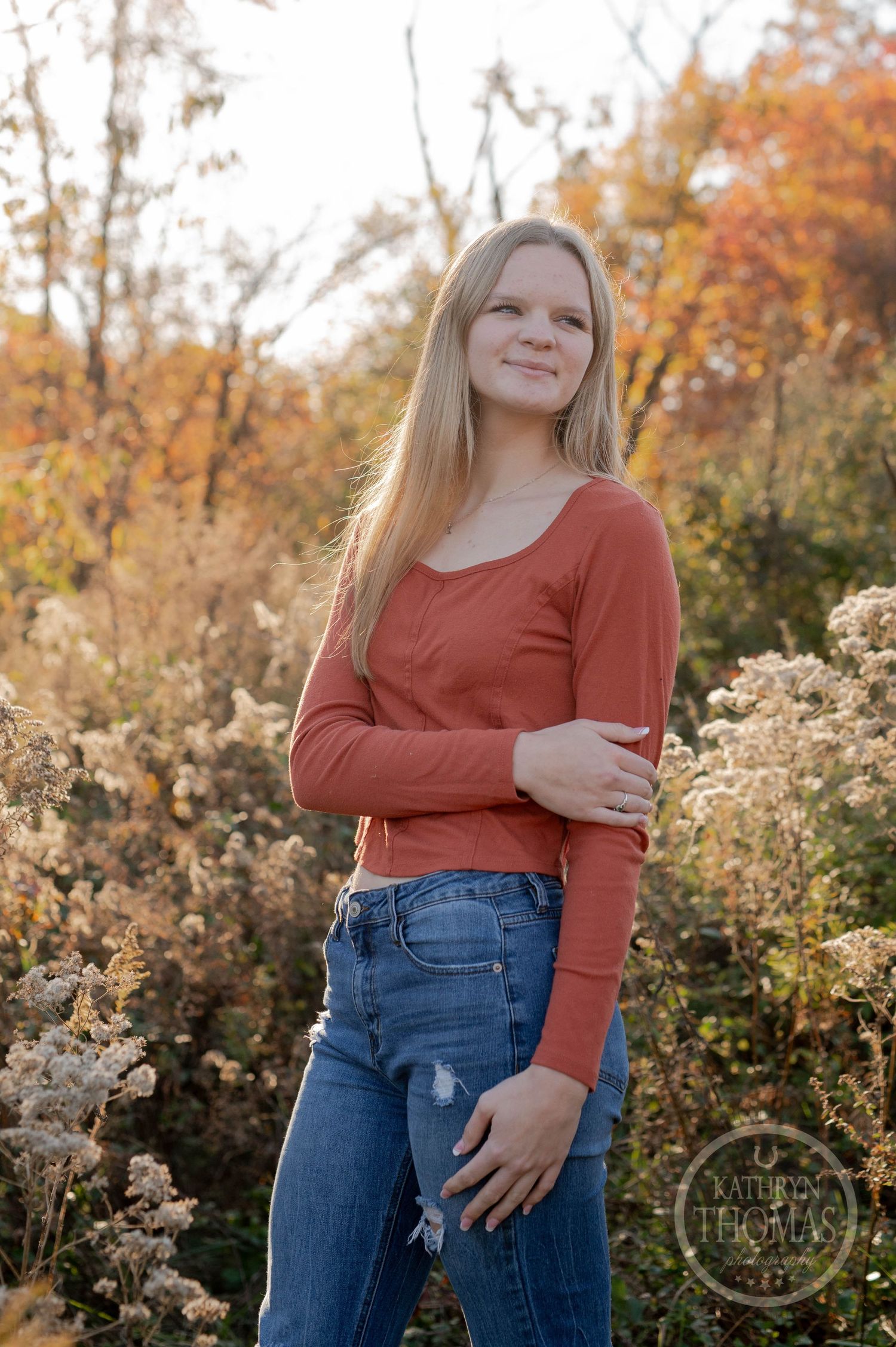 Portrait in a rustic fall setting with dried wildflowers and autumn trees in golden light.