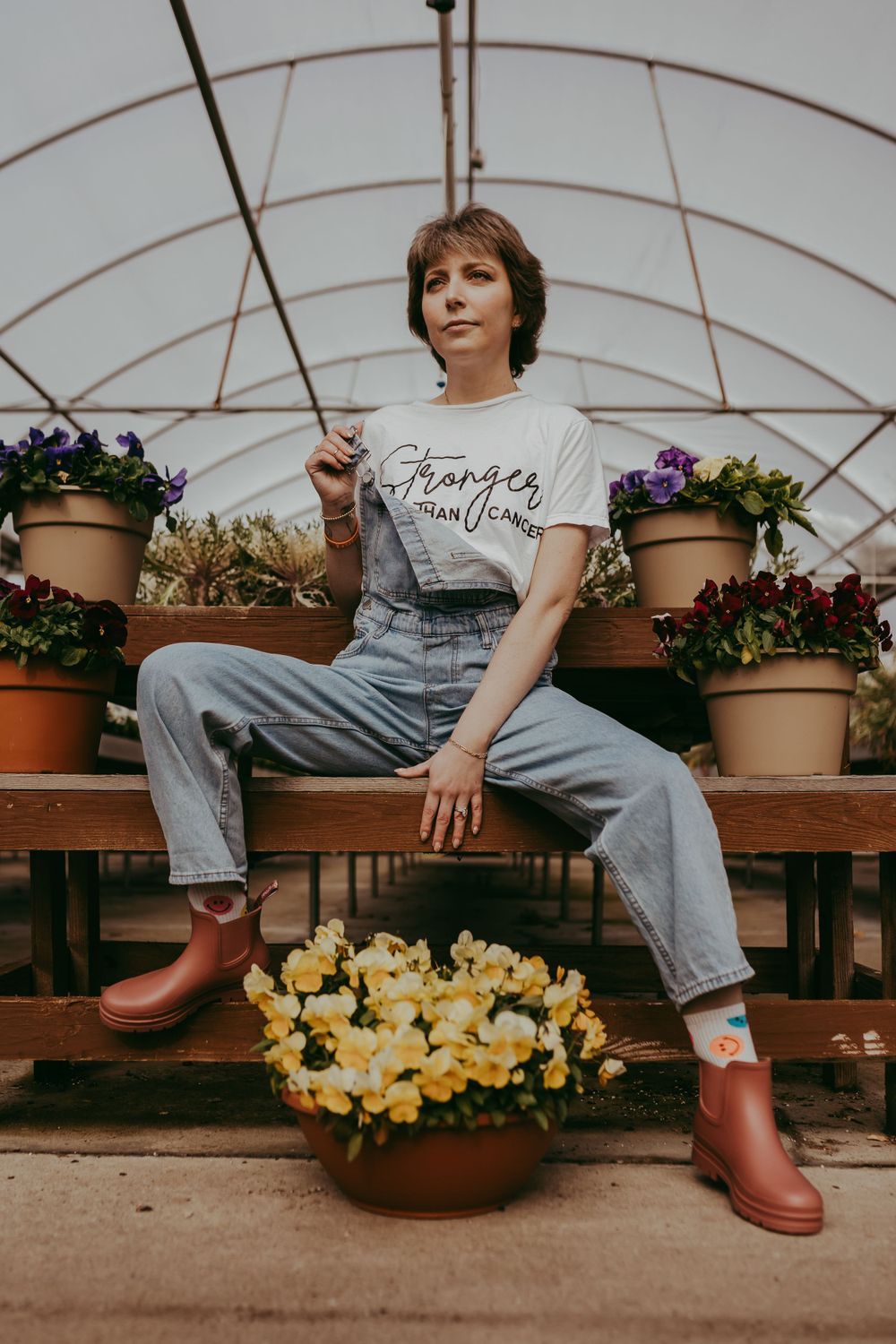 Casual garden scene with denim overalls and red rain boots among potted yellow daffodils in a greenhouse.