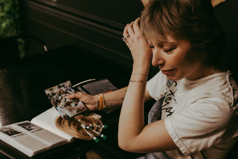 Person sits at a desk reading a book in moody lighting with hands clasped near their face.