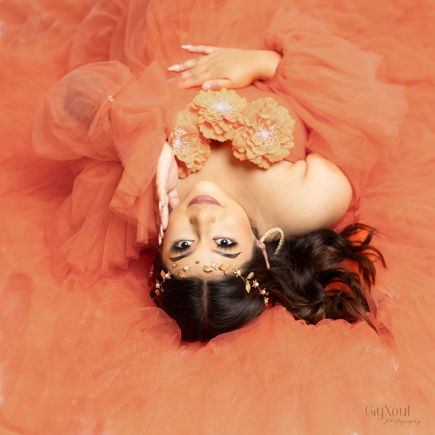 Woman in peach-colored tulle dress lying gracefully in artistic boudoir photo series.