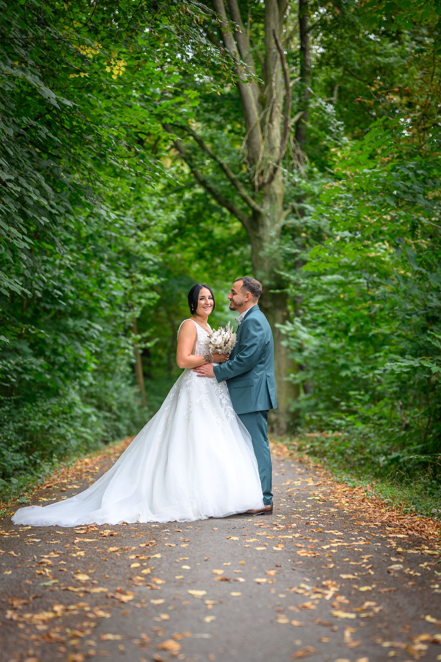 Wedding couple poses romantically by ornate iron gate during golden hour.