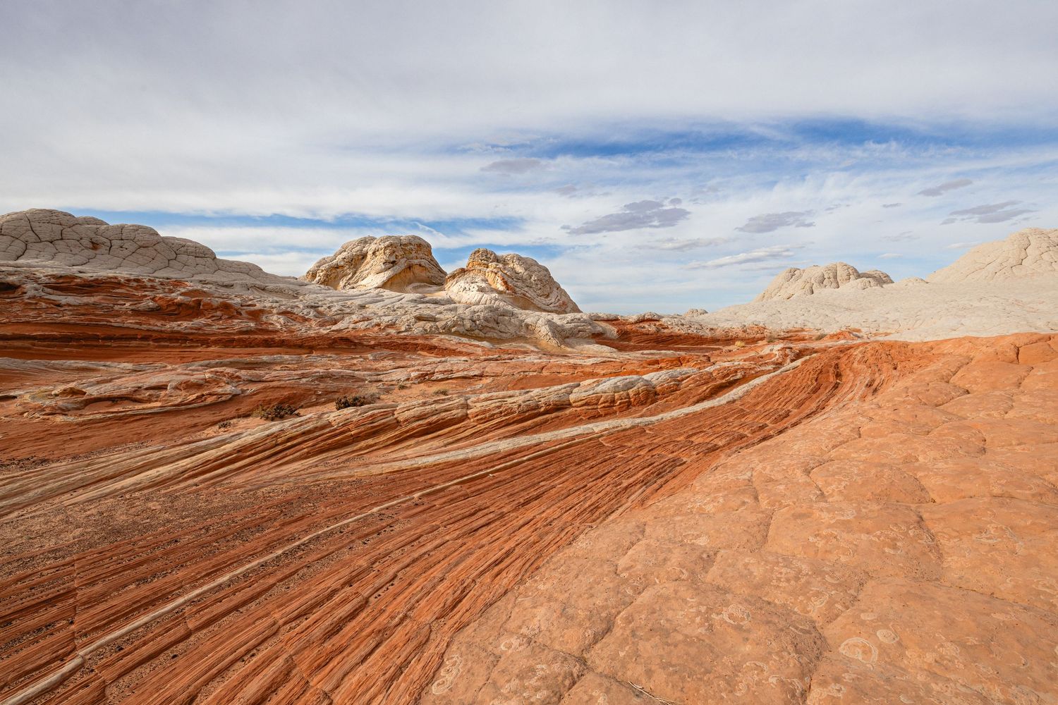 Swirling red sandstone formations create dramatic patterns in a desert landscape under cloudy skies.