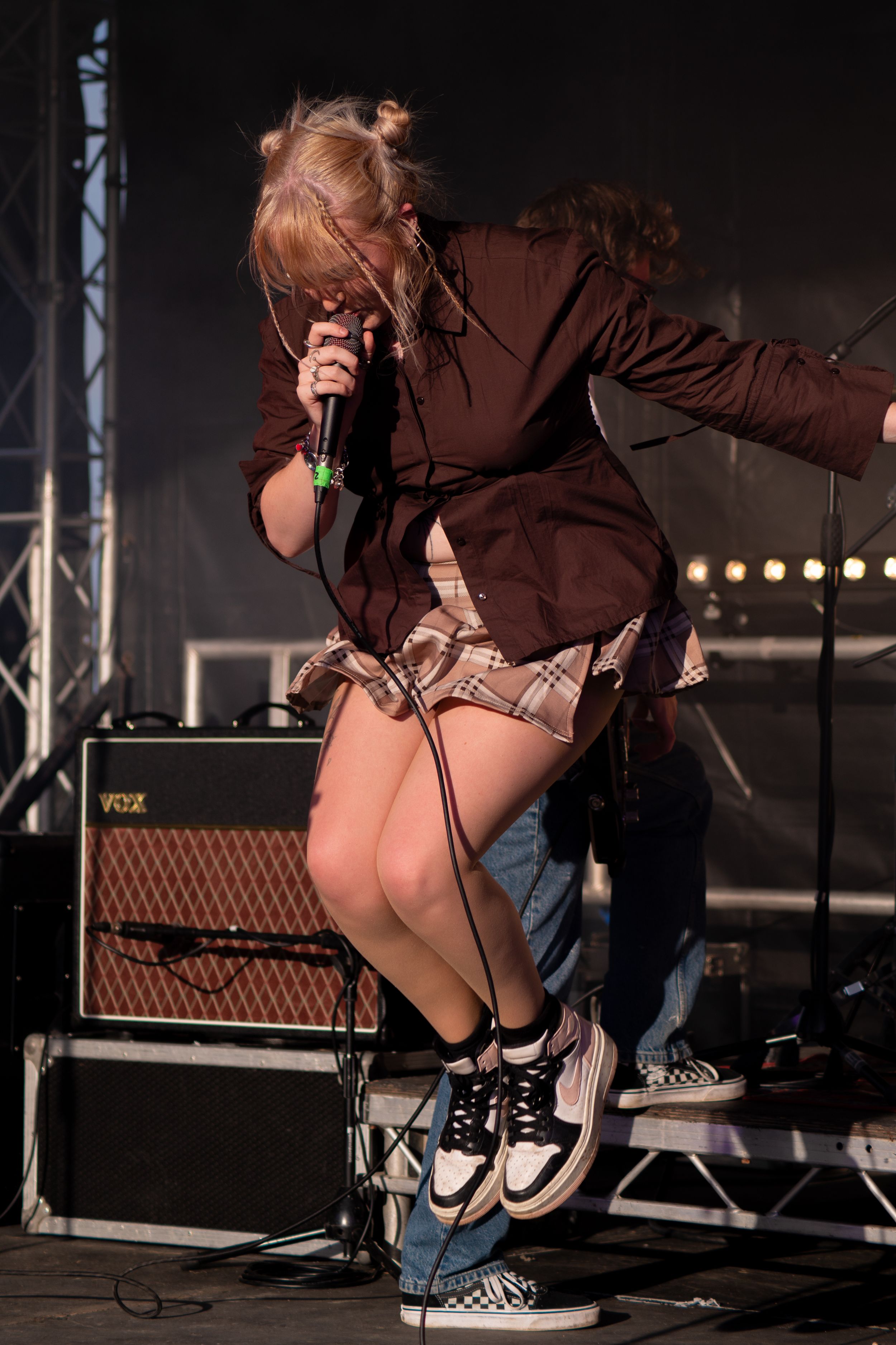 Performer crouches on stage during concert with guitar amplifier and stage lights visible in background.