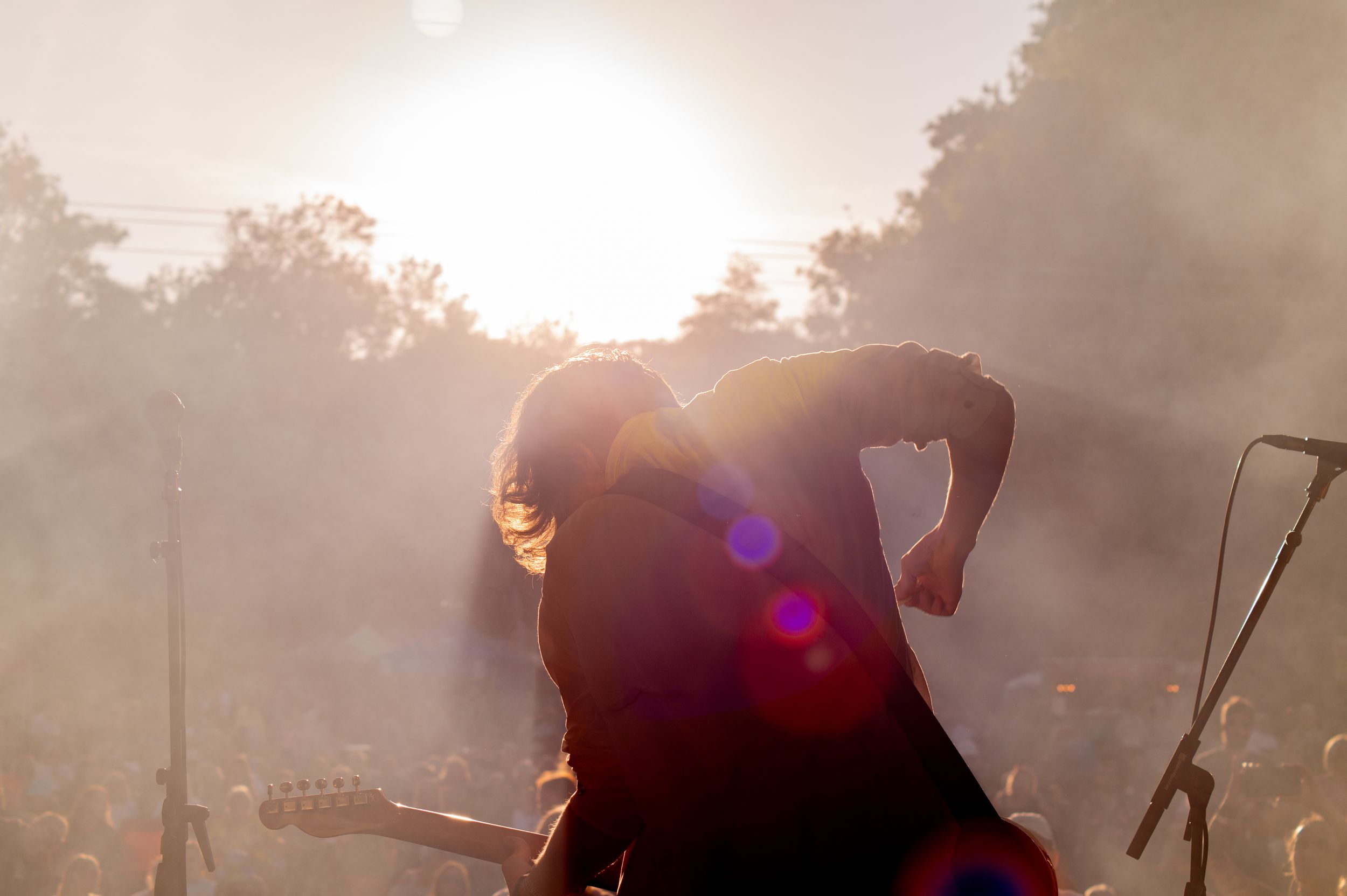 A silhouetted guitarist performs on stage against a dramatic sunset backdrop with lens flare effects.