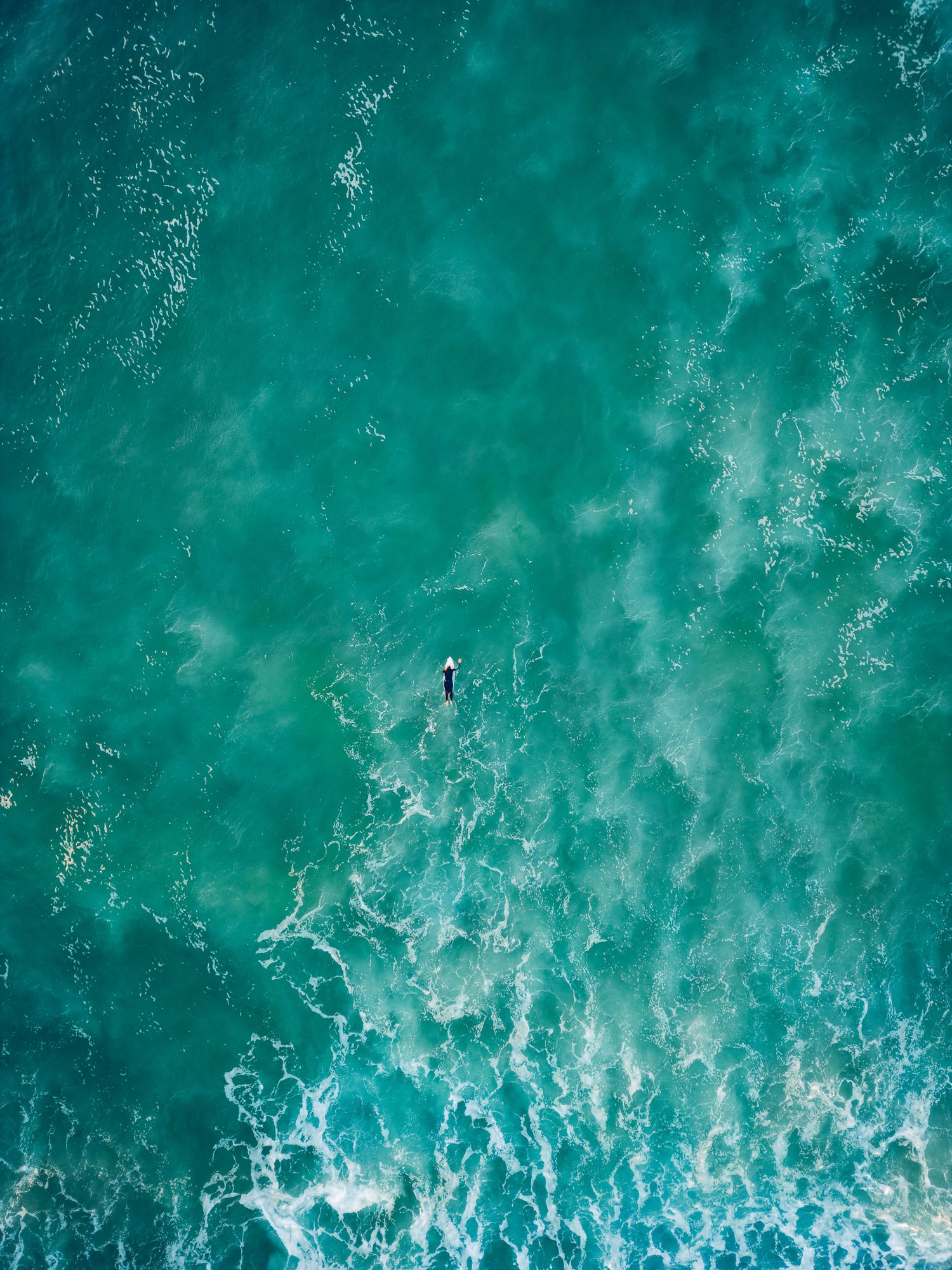 Vue aérienne des surfeurs flottant sur des planches de surf dans l'eau profonde de l'océan turquoise.