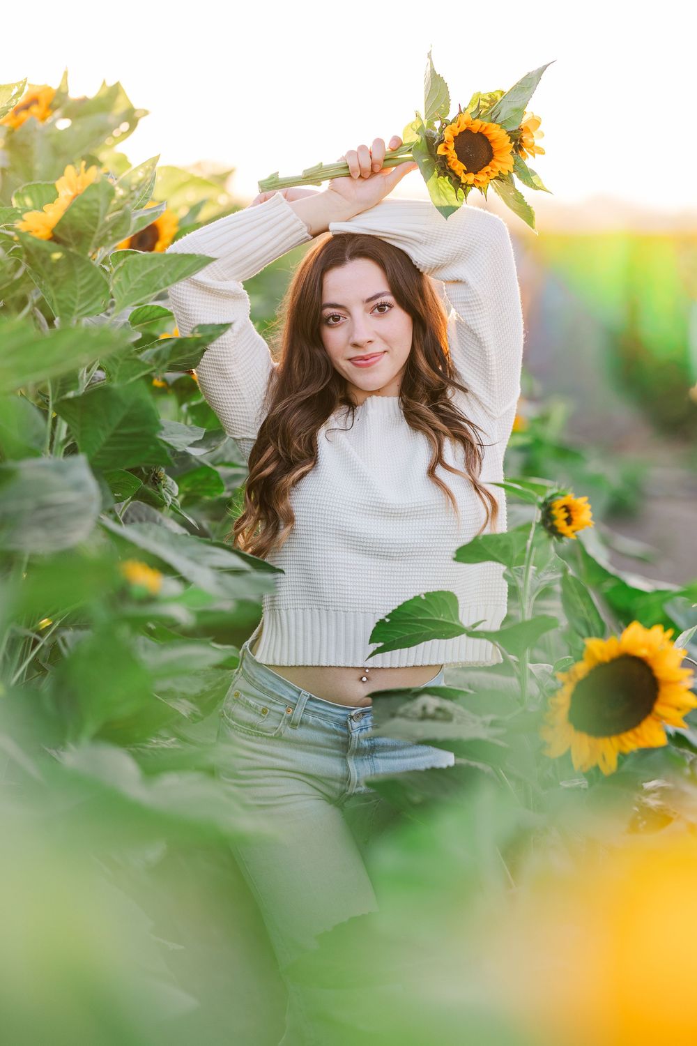A playful summer portrait amidst tall sunflowers features a white sweater and casual style in golden evening light.
