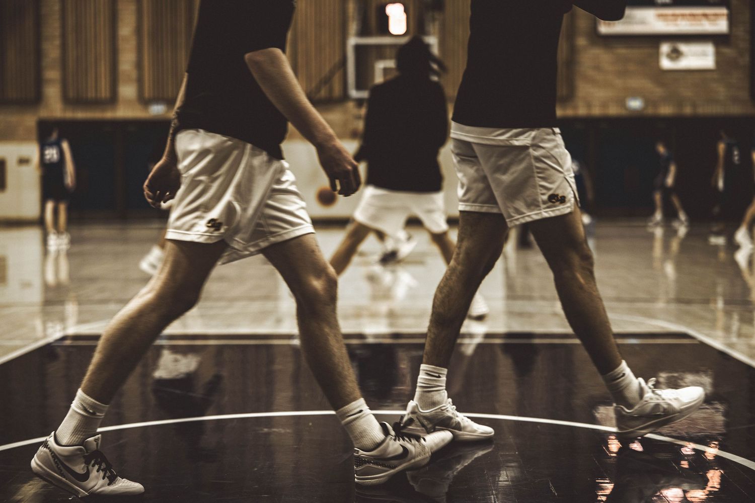 Basketball players in white shorts compete on a polished indoor court.