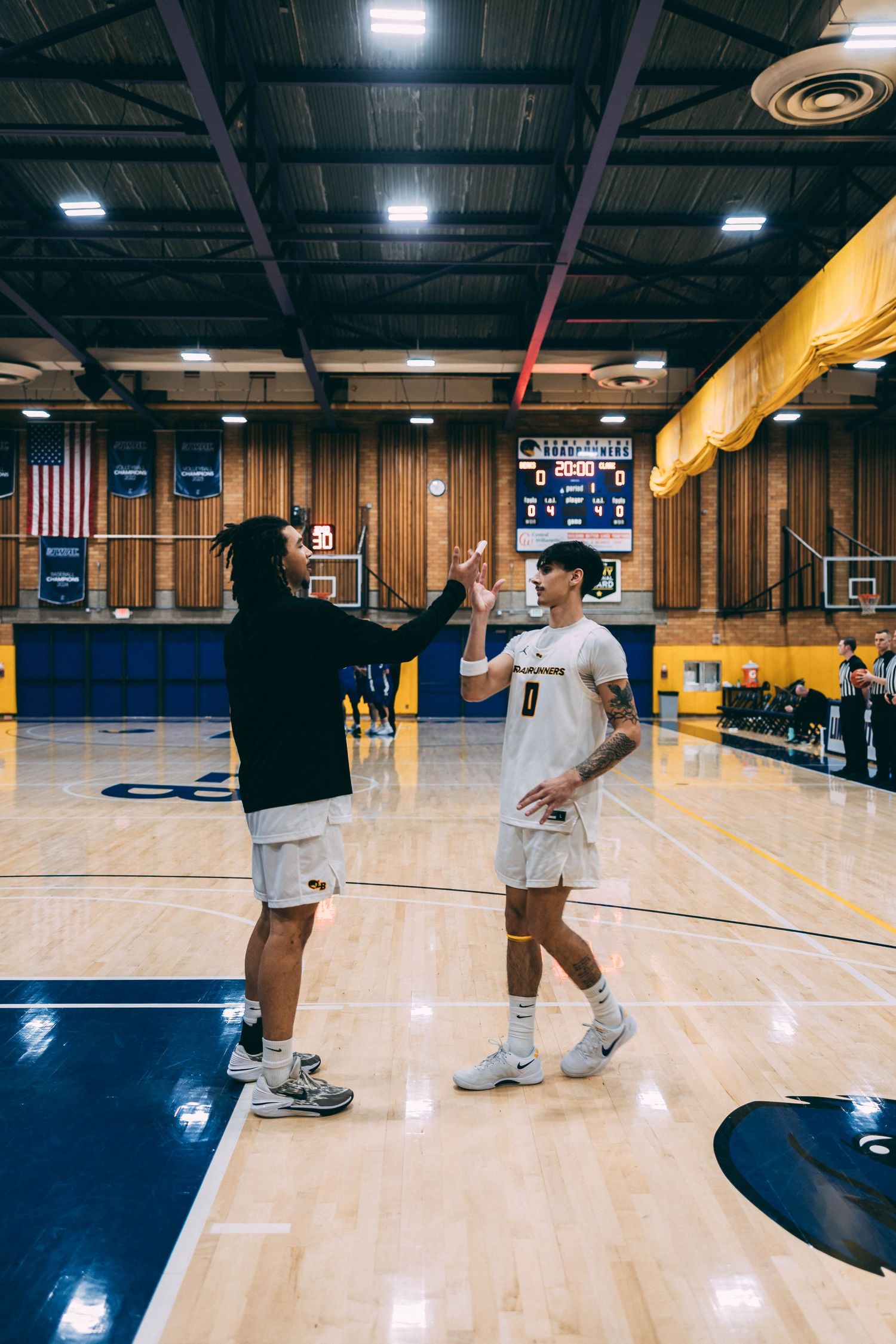Players practice basketball drills on polished court with American flag visible in background.