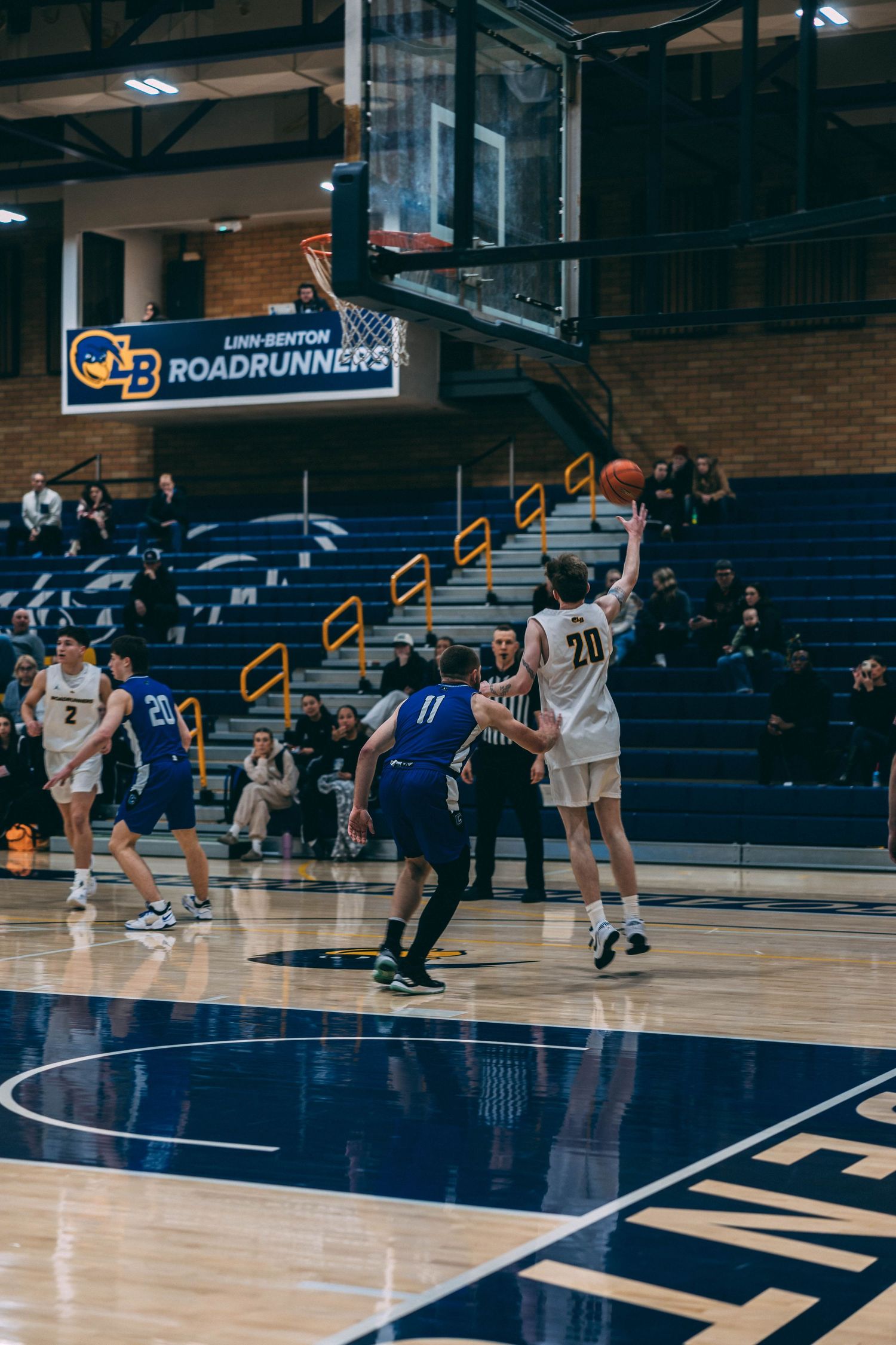 Basketball game in progress on indoor court with players in white and blue uniforms.